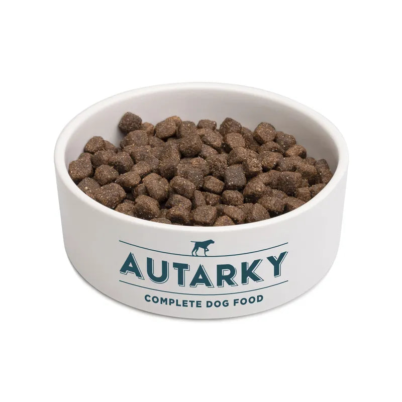 White bowl filled with Autarky complete dog food on a white background